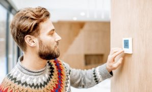 Man in sweater feeling cold adjusting room temperature with electronic thermostat at home